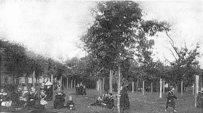 black and white photo of girls in school uniforms with nuns in habits playing in the Abbey garden, background of trees