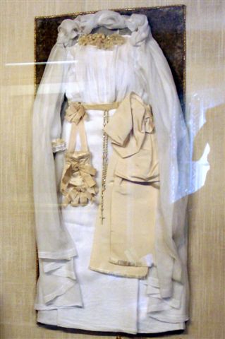color photo of white dress and veil worn by St. Therese the Little Flower on her First Communion Day, rosary hanging from the waist
