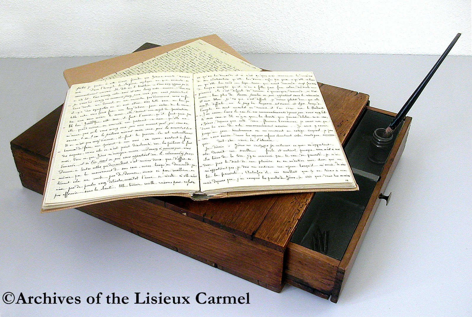 color photo of small wooden writing-desk (a lap desk) on which Therese wrote her manuscripts.  Manuscripts open on top.  An open drawer shows pen, inkstand, and spare nibs
