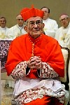 Cardinal Loris Francesco Capovilla, seated, in red robes as a cardinal, among other ecclesiastics dressed in white.  He is applauding.