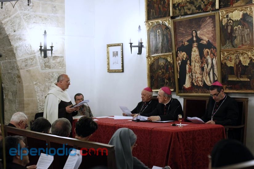 Fr. Antonio Sangalli, vice-postulator, in brown Carmelite habit and white cloak, reading a document.  A bishop in red skullcap sits behind a table with a red cloth